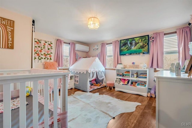 bedroom with a wall mounted air conditioner, wood-type flooring, and multiple windows