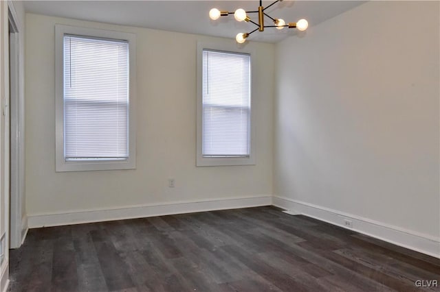 spare room featuring dark wood-type flooring and a notable chandelier