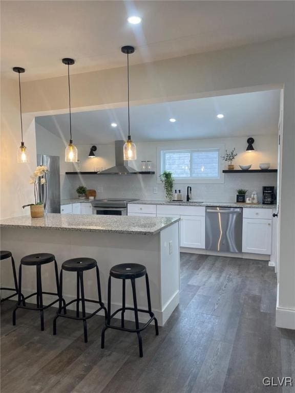 kitchen featuring a breakfast bar, white cabinetry, light stone counters, stainless steel appliances, and wall chimney exhaust hood