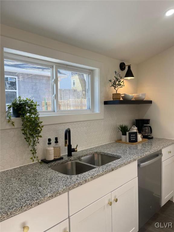 kitchen with dishwasher, sink, white cabinets, decorative backsplash, and light stone counters