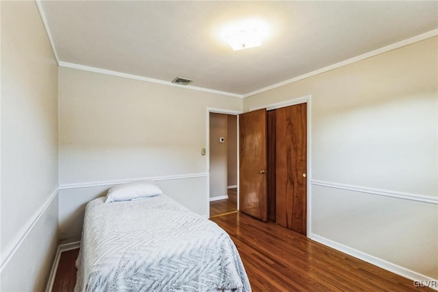 bedroom with dark wood-type flooring, crown molding, and a closet