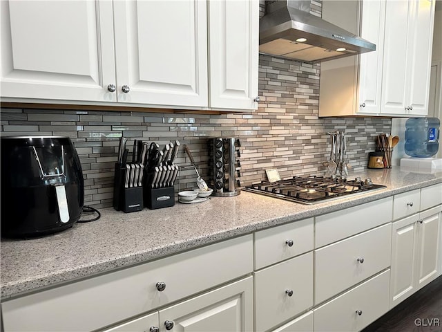 kitchen with light stone counters, white cabinets, stainless steel gas stovetop, and wall chimney range hood