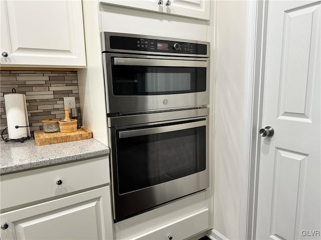 kitchen featuring white cabinetry, light stone countertops, double oven, and tasteful backsplash