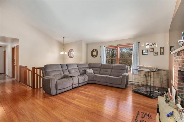 living room with a brick fireplace, a notable chandelier, vaulted ceiling, and hardwood / wood-style floors