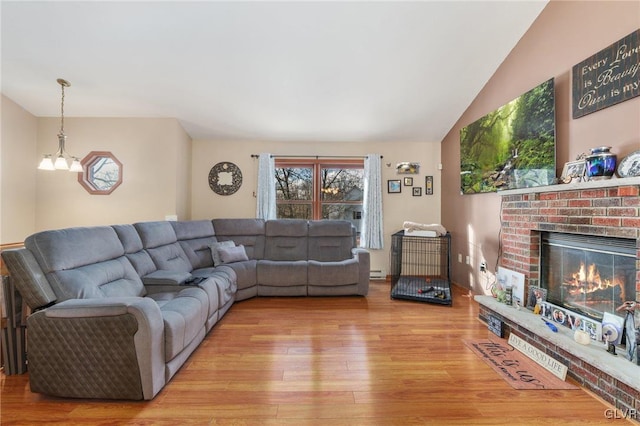 living room featuring a brick fireplace, vaulted ceiling, light hardwood / wood-style floors, and a chandelier