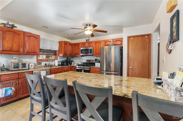 kitchen featuring sink, tasteful backsplash, appliances with stainless steel finishes, a kitchen breakfast bar, and light stone countertops