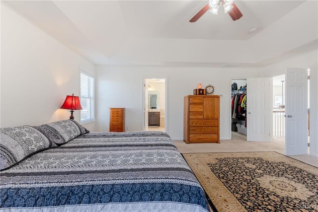 bedroom featuring connected bathroom, a spacious closet, a tray ceiling, light carpet, and a closet