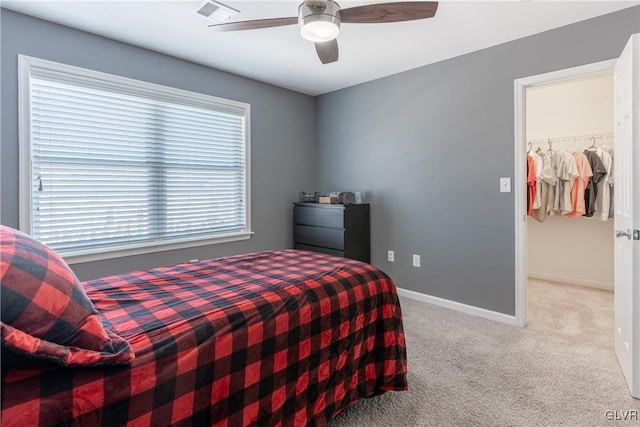 bedroom with a walk in closet, light carpet, and ceiling fan