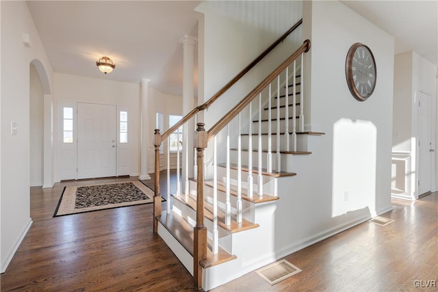 foyer entrance featuring dark wood-type flooring, plenty of natural light, and ornate columns