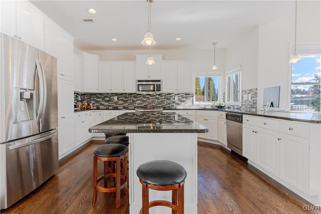 kitchen with stainless steel appliances, white cabinetry, a kitchen island, and a breakfast bar area