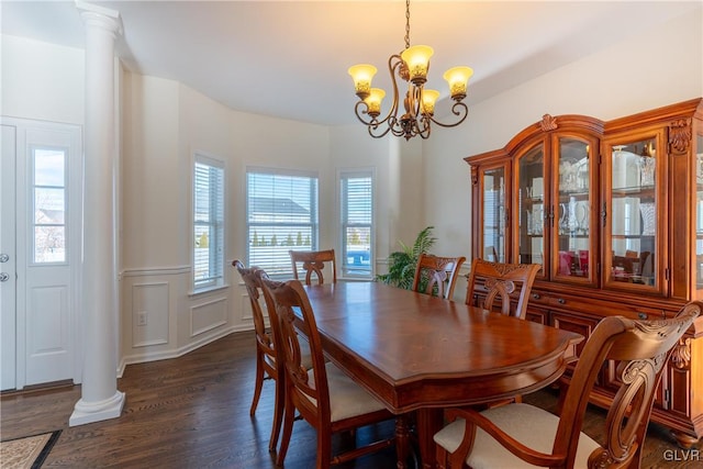 dining room featuring ornate columns, a healthy amount of sunlight, dark wood-type flooring, and a chandelier