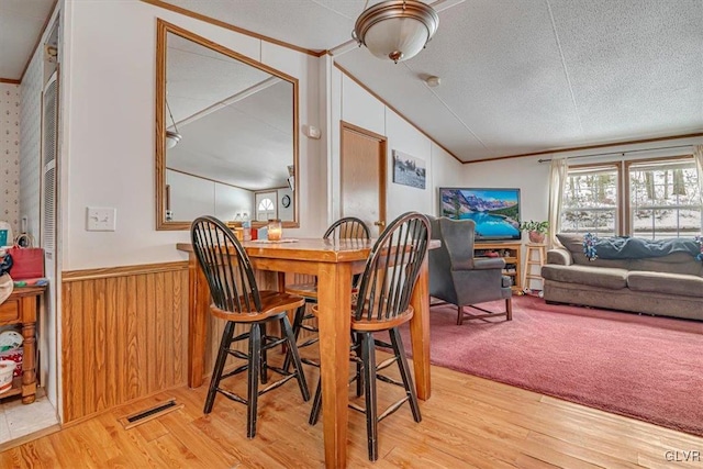 dining space featuring vaulted ceiling, ornamental molding, a textured ceiling, and light wood-type flooring