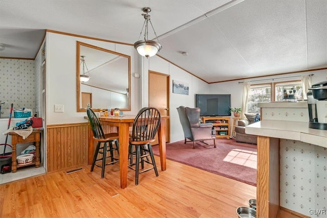 dining area with ornamental molding, wooden walls, light hardwood / wood-style floors, and vaulted ceiling