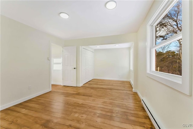 unfurnished room with a baseboard heating unit and light wood-type flooring