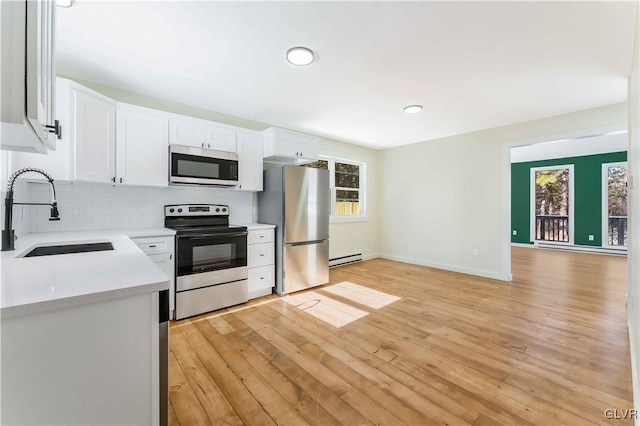 kitchen with sink, appliances with stainless steel finishes, backsplash, white cabinets, and light wood-type flooring