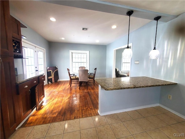 kitchen with kitchen peninsula, light tile patterned floors, hanging light fixtures, and dark stone countertops