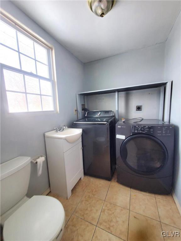 clothes washing area featuring washer and clothes dryer, sink, and light tile patterned floors