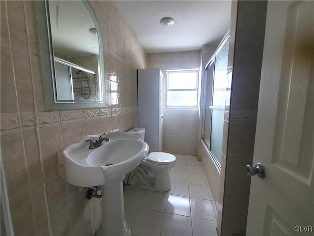 full bathroom featuring tile patterned floors, toilet, sink, combined bath / shower with glass door, and tile walls