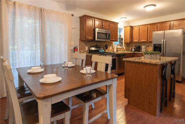 kitchen with tasteful backsplash, appliances with stainless steel finishes, dark hardwood / wood-style flooring, a kitchen island, and dark stone counters