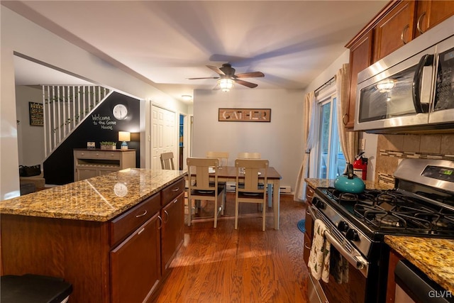 kitchen with ceiling fan, appliances with stainless steel finishes, light stone counters, tasteful backsplash, and dark hardwood / wood-style flooring