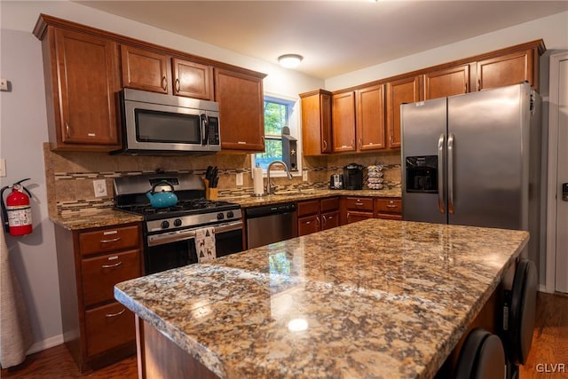 kitchen with a kitchen island, light stone countertops, appliances with stainless steel finishes, and decorative backsplash