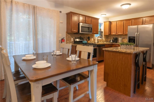 kitchen with appliances with stainless steel finishes, hardwood / wood-style floors, tasteful backsplash, dark stone counters, and a center island