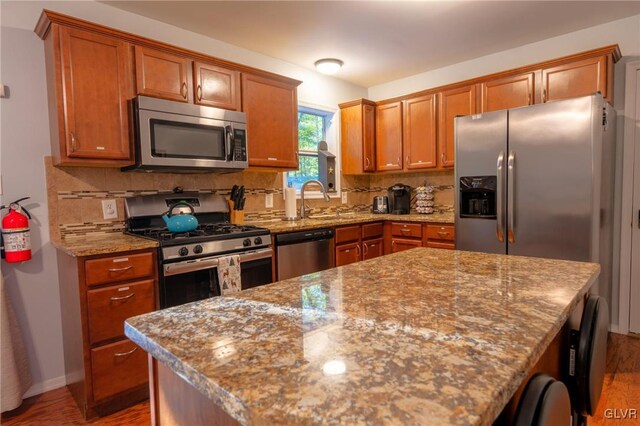 kitchen featuring sink, light stone counters, appliances with stainless steel finishes, hardwood / wood-style flooring, and backsplash