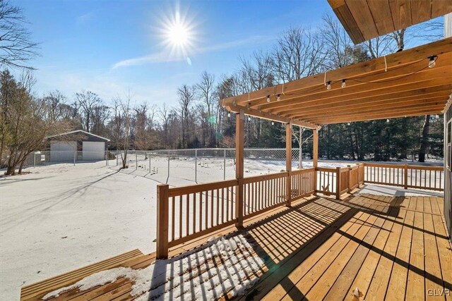 snow covered deck with an outbuilding, a garage, and a pergola