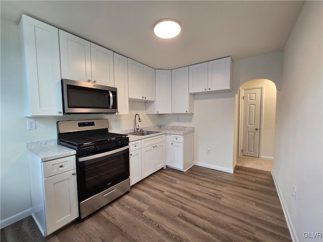 kitchen with sink, white cabinetry, dark hardwood / wood-style flooring, stainless steel appliances, and light stone countertops