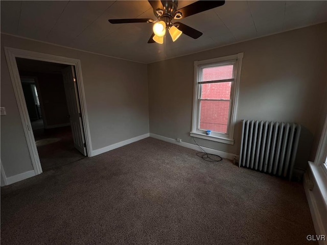 spare room featuring ceiling fan, radiator, and dark colored carpet