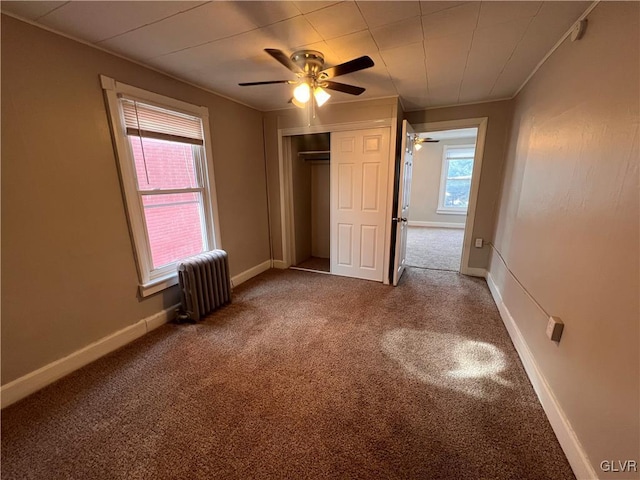 unfurnished bedroom featuring crown molding, carpet flooring, radiator, a closet, and ceiling fan