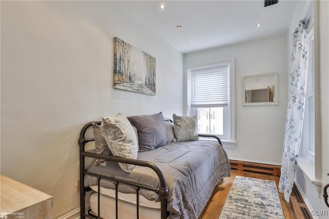 bedroom with light hardwood / wood-style floors and a baseboard heating unit