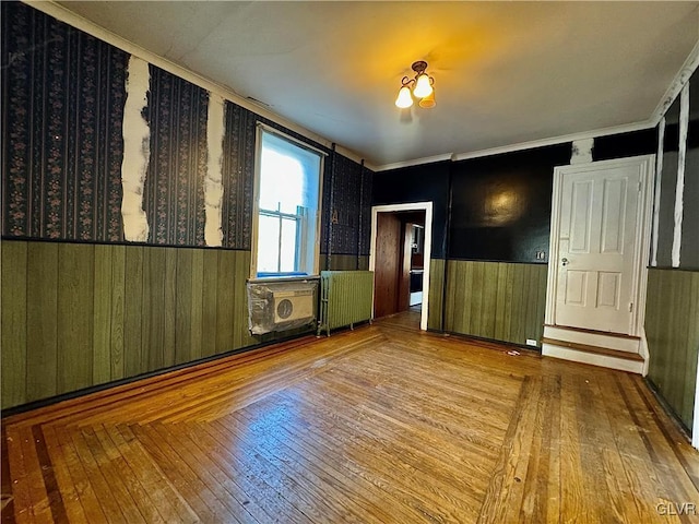 unfurnished room with wood-type flooring, radiator heating unit, and wood walls