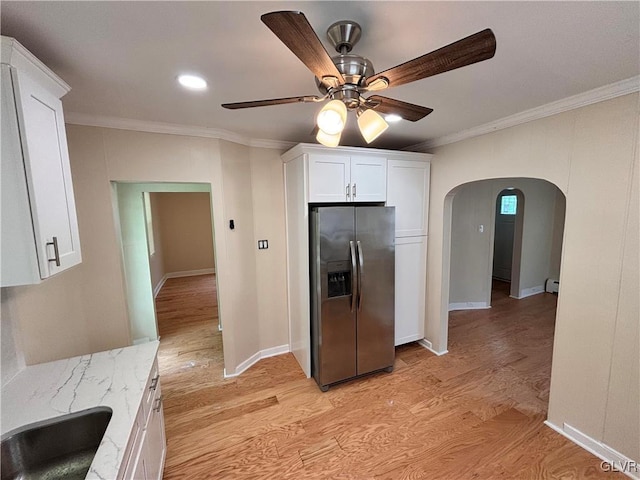 kitchen with crown molding, stainless steel fridge, light stone countertops, white cabinets, and light wood-type flooring