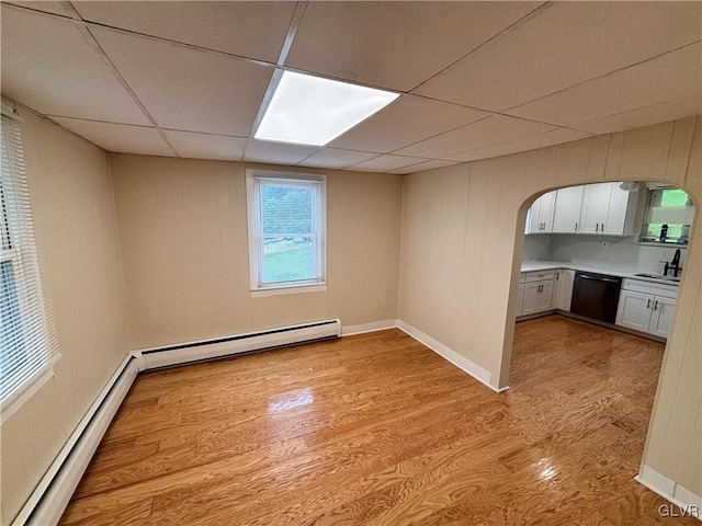 interior space with a baseboard heating unit, a paneled ceiling, sink, and light wood-type flooring