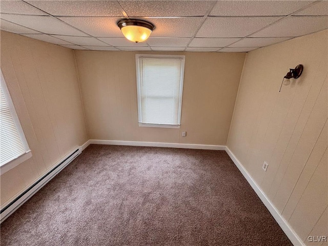 carpeted empty room featuring a drop ceiling, wooden walls, and baseboard heating