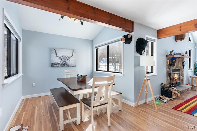 dining room featuring rail lighting, vaulted ceiling with beams, a fireplace, and light hardwood / wood-style floors