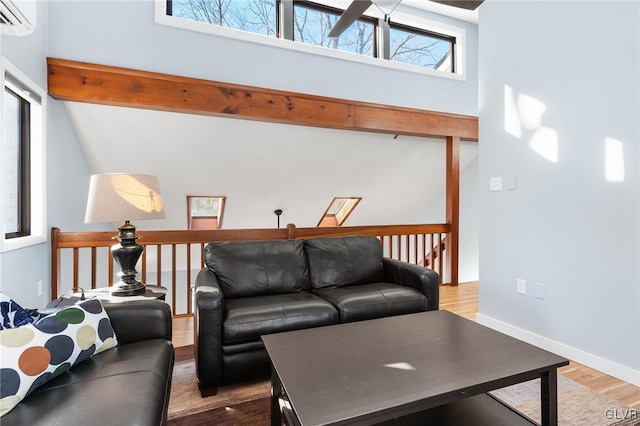 living room featuring hardwood / wood-style flooring, a towering ceiling, a wall mounted air conditioner, and beam ceiling