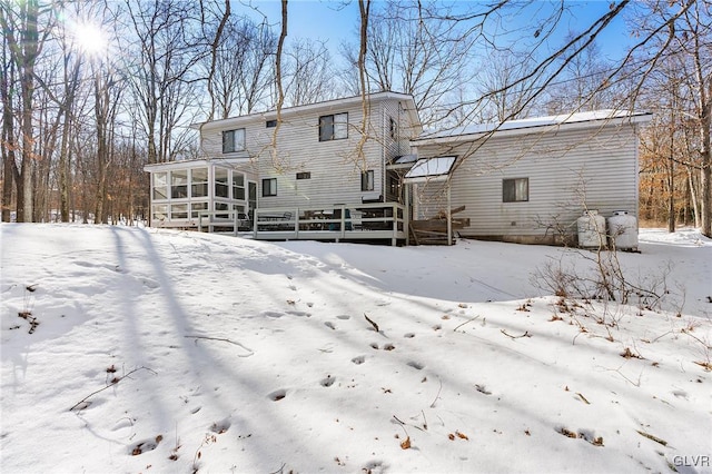 snow covered rear of property featuring a sunroom