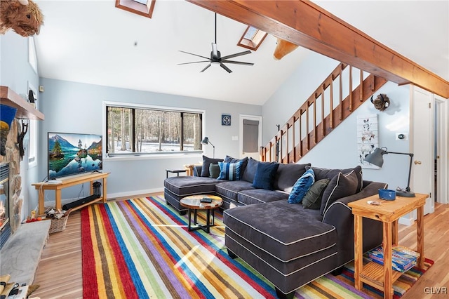 living room with ceiling fan, a fireplace, light hardwood / wood-style floors, and vaulted ceiling with skylight