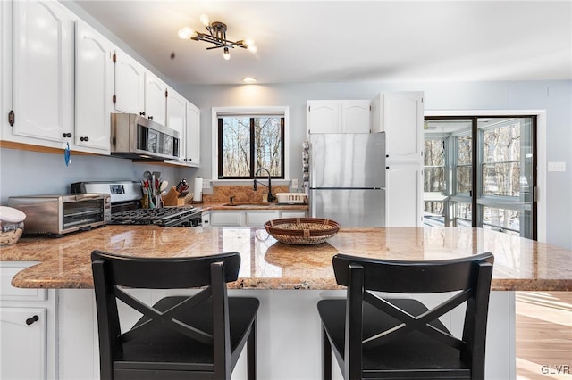 kitchen with white cabinetry, appliances with stainless steel finishes, sink, and a kitchen bar