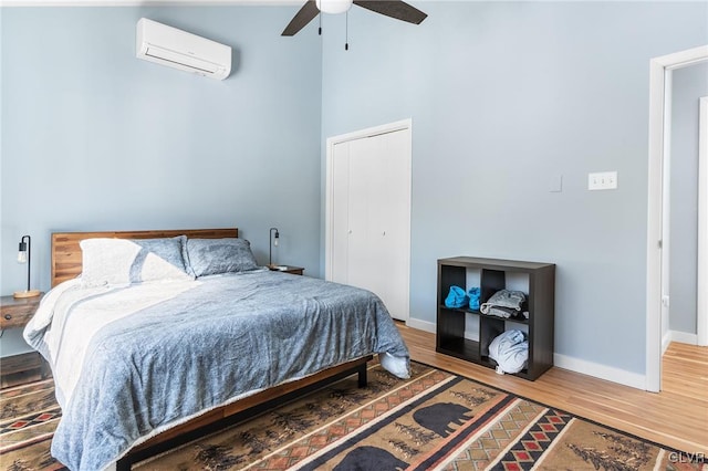 bedroom with a high ceiling, an AC wall unit, hardwood / wood-style floors, and ceiling fan