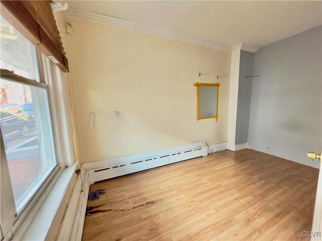 empty room featuring crown molding, light hardwood / wood-style flooring, and a baseboard heating unit