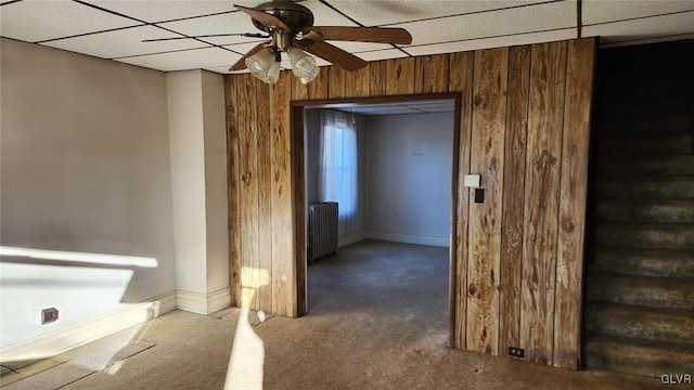 interior space with a paneled ceiling, radiator heating unit, ceiling fan, and wood walls