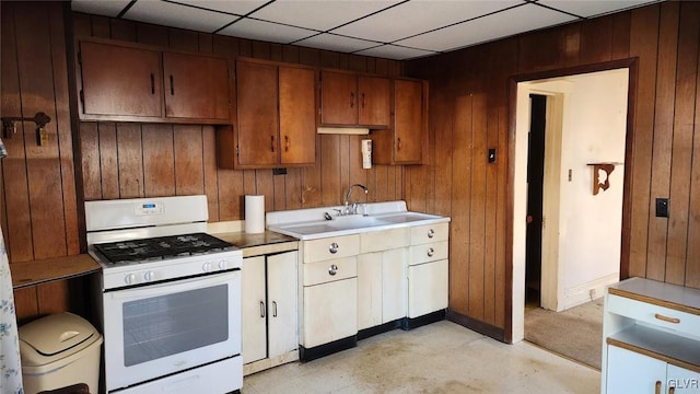 kitchen featuring a drop ceiling, white range with gas stovetop, and wood walls