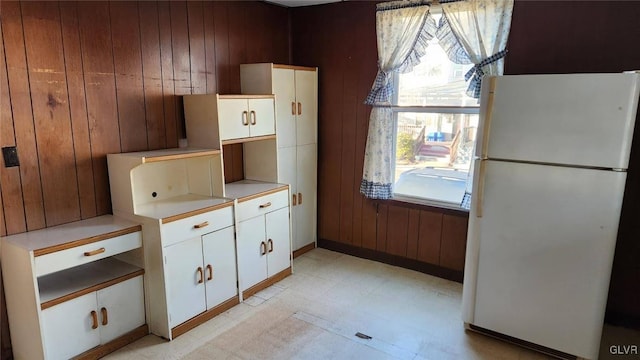 kitchen with white fridge, a healthy amount of sunlight, white cabinets, and wooden walls