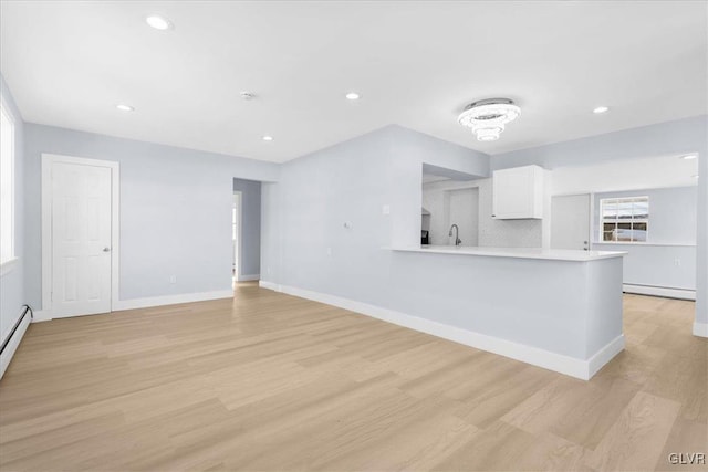 unfurnished living room with a baseboard heating unit, sink, and light wood-type flooring