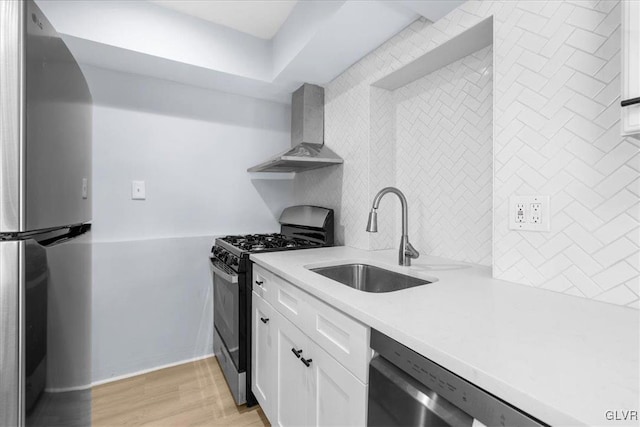 kitchen with wall chimney range hood, sink, light hardwood / wood-style flooring, stainless steel appliances, and white cabinets