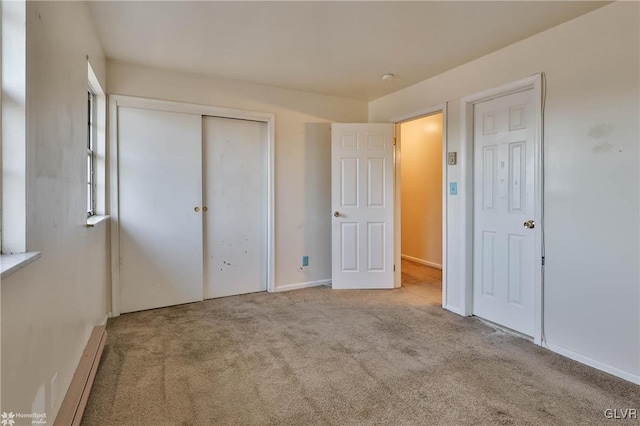 unfurnished bedroom with light colored carpet, a closet, and a baseboard heating unit