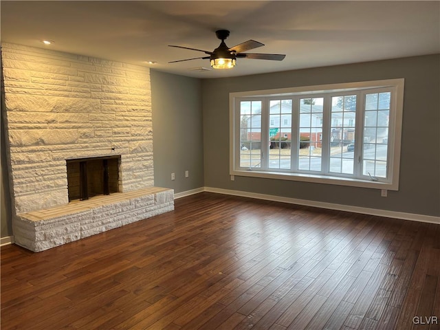 unfurnished living room featuring a stone fireplace, dark hardwood / wood-style floors, and ceiling fan